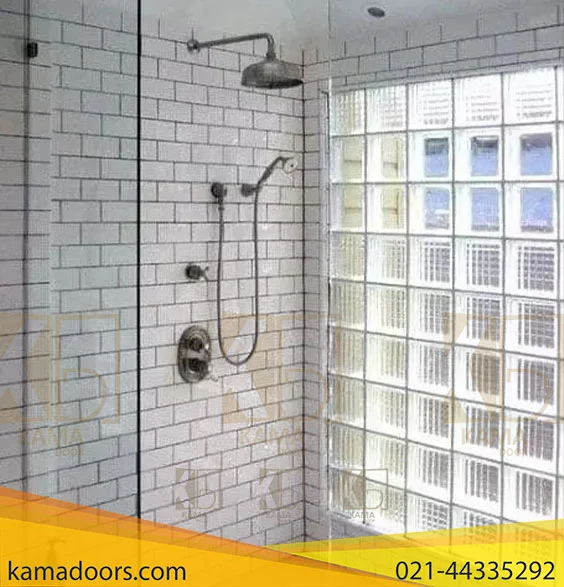 یک دوش مدرن با درب های شیشه ای و دیوارهای کاشی کاری شده سفید را به تصویر می کشد. قسمت دوش توسط یک درب شیشه ای با دستگیره های فلزی محصور شده است و یک دیوار شیشه ای دیگر در سمت راست قابل مشاهده است. در داخل دوش، دو سر دوش وجود دارد: یک سر دوش از جنس استیل ضد زنگ و یک سر دوش قابل تنظیم که به دیوار متصل است. کنترل های تنظیم دما و جریان آب نیز روی دیوار قابل مشاهده است. دیوارهای دوش با کاشی های کوچک مربعی و سفید پوشانده شده است که ظاهری تمیز و مدرن به آن بخشیده است. در سمت راست، خارج از محوطه دوش، دیوار دیگری پوشیده شده با کاشی‌ های مربعی کوچک مشابه وجود دارد که به نظر می‌رسد از شیشه ساخته شده‌اند یا پوششی براق دارند. به طور کلی، این یک طراحی حمام براق و امروزی است.