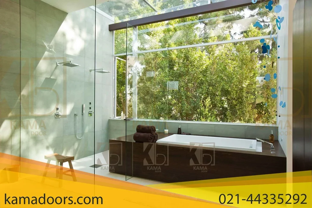 یک حمام مدرن با پنجره‌ای بزرگ است که منظره‌ ای از فضای سبز بیرون را ارائه می‌ دهد. حمام دارای عناصر طراحی معاصر با خطوط تمیز و سبکی ساده است. یک وان بزرگ مستطیلی در کنار پنجره‌ ای از کف تا سقف قرار دارد که نور طبیعی فراوان و منظره‌ ای از برگ‌ های سبز را فراهم می‌ کند. یک محفظه دوش شیشه‌ ای طراحی شده توسط کامادر در کنار وان قرار دارد، که هم دوش دستی و هم دوش بارانی بالاسری در آن قابل مشاهده است. یک کابینت چوبی تیره زیر پنجره وان را پشتیبانی می‌ کند و روی آن حوله‌ ای تیره به طور مرتب تا شده است. در سمت چپ وان، یک صندلی کوچک چوبی با وسایل بهداشتی روی آن قرار دارد. روی کف جلوی وان، یک پادری یا قالیچه حمام سفید قرار دارد که گرما به فضا می‌ بخشد. دیوار ها با کاشی‌ های بزرگ و روشن پوشیده شده‌ اند که به حس روشن و هوایی اتاق کمک می‌ کنند.