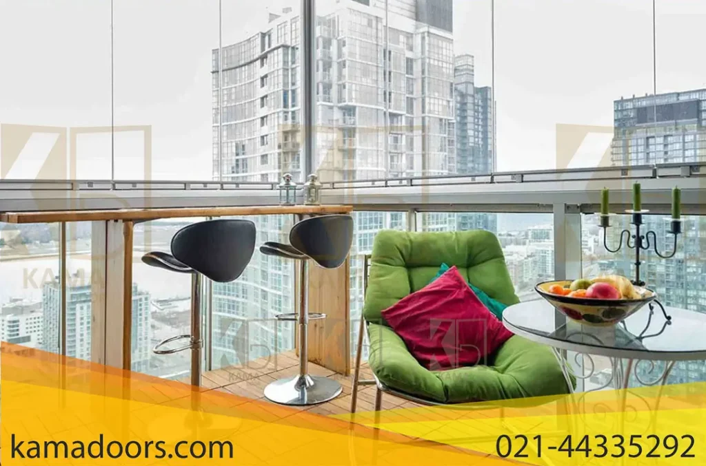 نشان دهنده یک بالکن مدرن با منظره‌ ای از ساختمان‌ های بلند است. مبلمان فضای باز شامل دو صندلی بار و یک میز گرد با رویه شیشه‌ ای و همچنین یک صندلی راحتی با کوسن سبز رنگ می‌ باشد. روی میز، کاسه‌ ای حاوی میوه‌ های مختلف قرار دارد و بالای آن چیزی شبیه به یک گیاه کوچک یا تزئینی آویزان است. بالکن دارای شیشه های بالکنی کامادر است که منظره‌ ای بدون مانع از چشم‌ انداز شهری را فراهم می‌ کند.