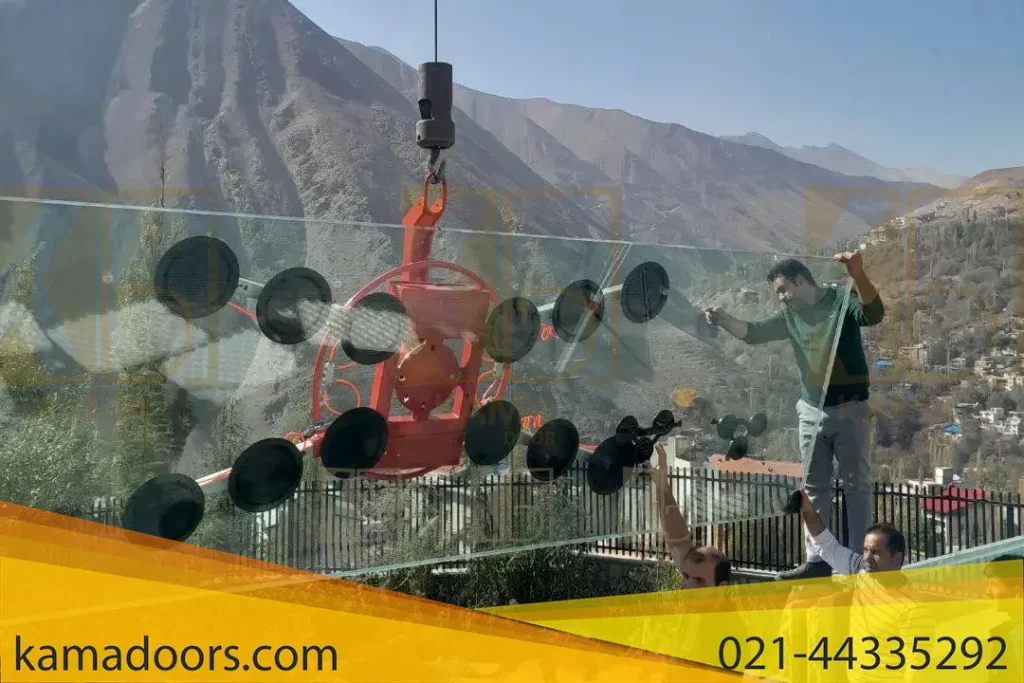یک صحنه کاری در یک پروژه ساختمانی را نشان می‌ دهد. سه نفر کارگر در حال کار هستند تا یک پنل شیشه‌ ای بزرگ را نصب یا جابجا کنند. این پنل شیشه‌ ای توسط یک دستگاه توسط تسمه‌ هایی به یک جرثقیل معلق شده است. کارگران تجهیزات حفاظتی نظیر دستکش‌ های ایمنی به دست دارند و با دقت در حال قرار دادن پنل شیشه‌ ای شیشه استخر شرکت کامادر هستند. این صحنه نشان‌دهنده تلاش و همکاری گروهی در یک پروژه ساختمانی است. دقت و تلاش این کارگران برای اطمینان از نصب صحیح و ایمن پنل شیشه‌ای در این محیط طبیعی خیره‌کننده، قابل توجه است.