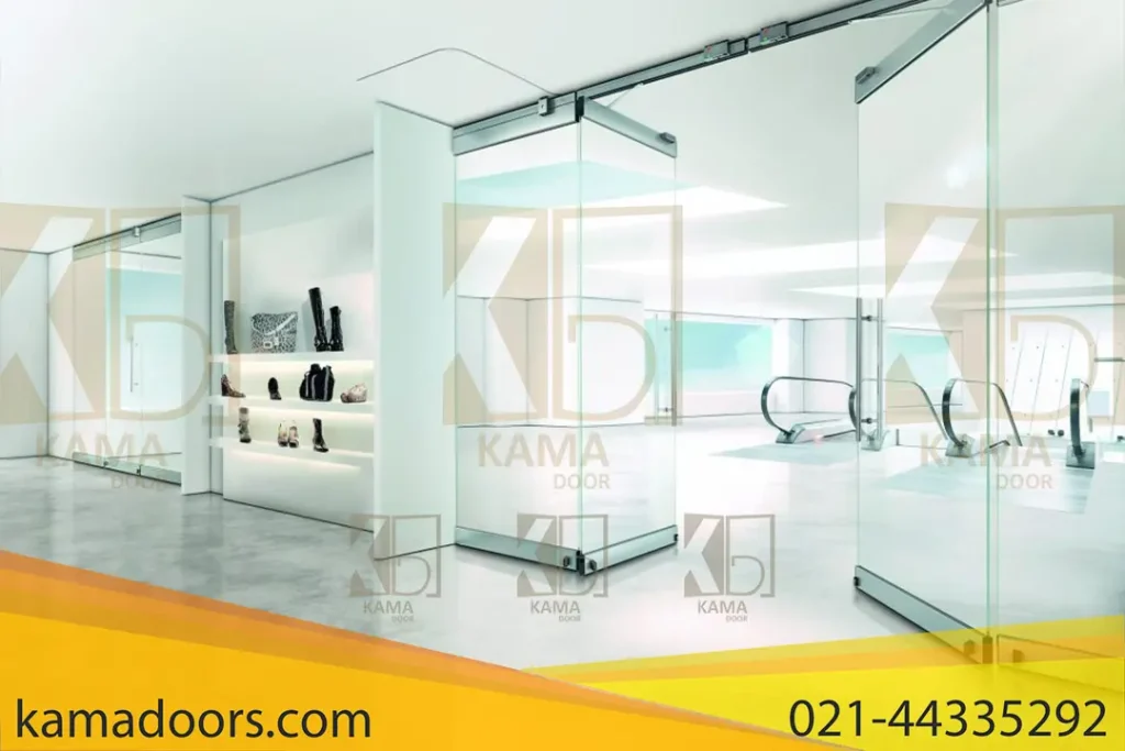 فضایی داخلی با طراحی مدرن و مینیمالیستی را نشان می‌ دهد. در سمت چپ، یک قفسه با کفش‌ ها و کیف‌ ها قرار دارد. در مرکز، پارتیشن های فولدینگ شیشه‌ ای کامادر دیده می‌ شود که به فضایی روشن و باز منتهی می‌ شوند. در پس‌ زمینه، پله‌ برقی‌ ها و دیوارهایی با طراحی ساده و شیشه‌ ای قابل مشاهده هستند. کفپوش این فضا از بتن صیقلی است و ترکیب نور طبیعی و مصنوعی جلوه‌ ای جذاب به فضا داده است. طراحی ساده و مدرن این تصویر حس پاکی و نظم را منتقل می‌ کند.